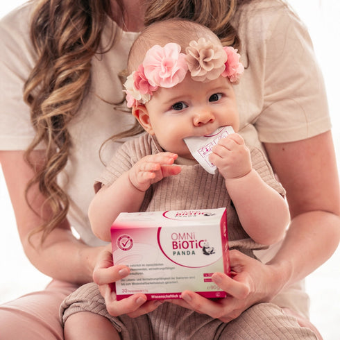 Ein Baby mit einer Packung OMNi-BiOTiC PANDA und einem Sachet im Mund